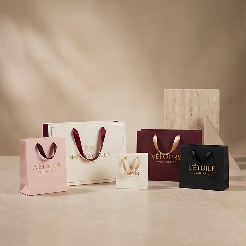 Six paper boutique bags in pink, cream, burgundy and black with ribbon handles and foil logos
