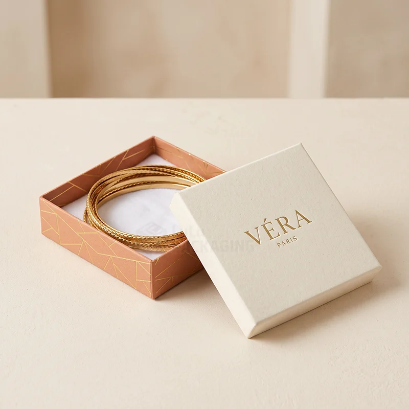 Cream lid and patterned base bracelet box holding a stack of gold bangles