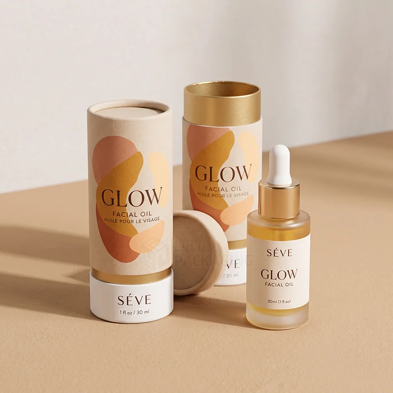 Two printed paper tube boxes with gold lining beside a facial oil dropper bottle