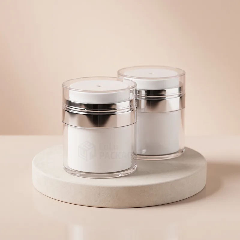 Two white airless jars with silver bands and clear lids on a round stone stand