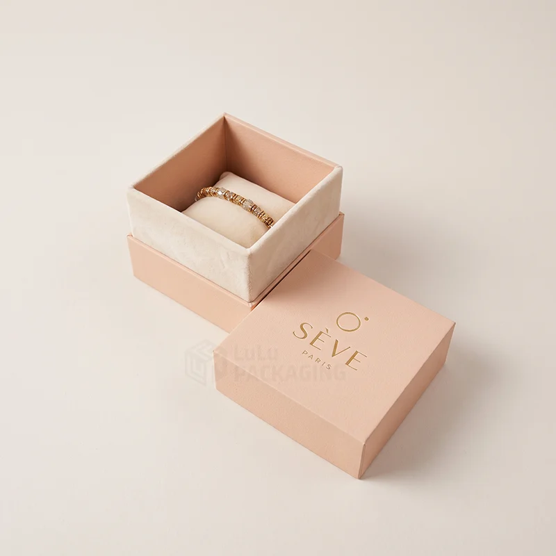 Peach bracelet box with a gold foil logo, open to show a beaded bracelet on a cushion