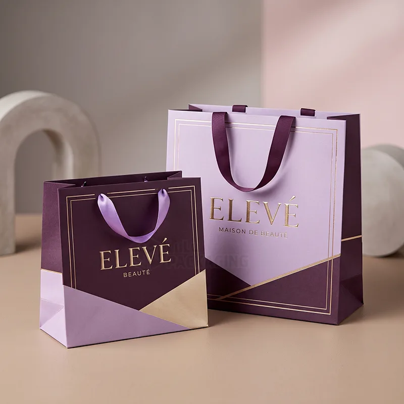 Two purple paper gift bags in small and large sizes with satin ribbon handles and gold foil logos