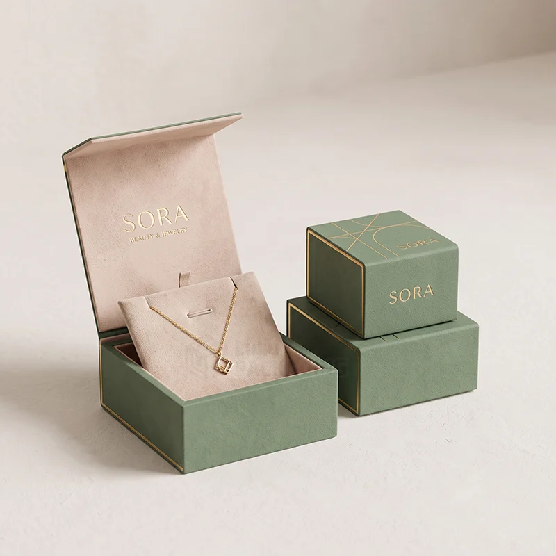 Sage green pendant boxes, one open with a pink suede pad holding a gold pendant necklace