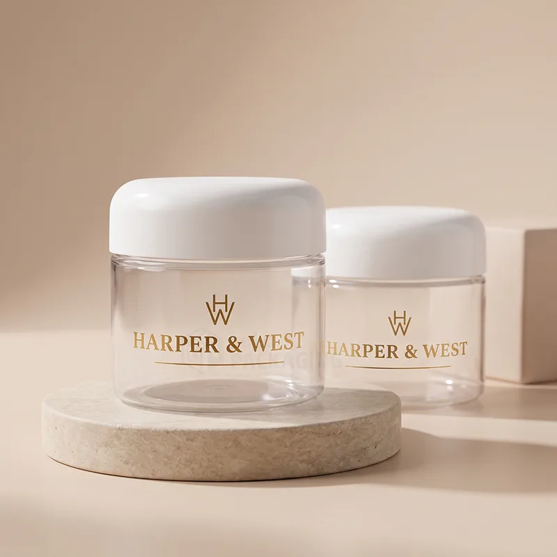 Two clear plastic cosmetic jars with white dome lids and gold printed logos