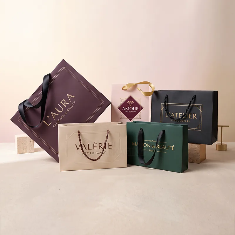 Five paper retail bags in plum, beige, pink, green and black with ribbon and rope handles