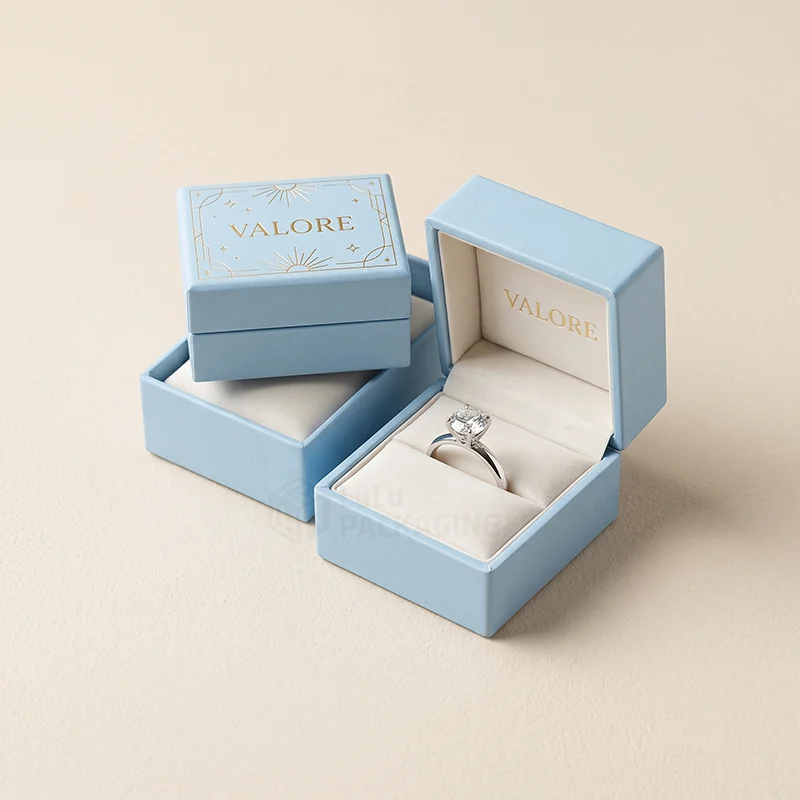 Light blue ring boxes with a gold foil logo, one open showing a diamond ring in a cream insert