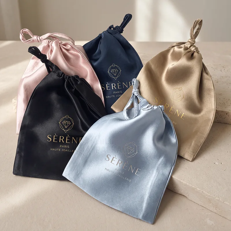 Five satin drawstring pouches in pink, black, navy, gold and light blue with a foil logo
