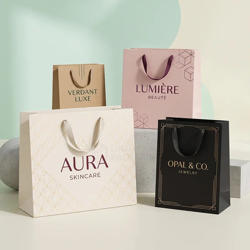 Four paper shopping bags in kraft, pink, cream and black with ribbon handles and printed logos