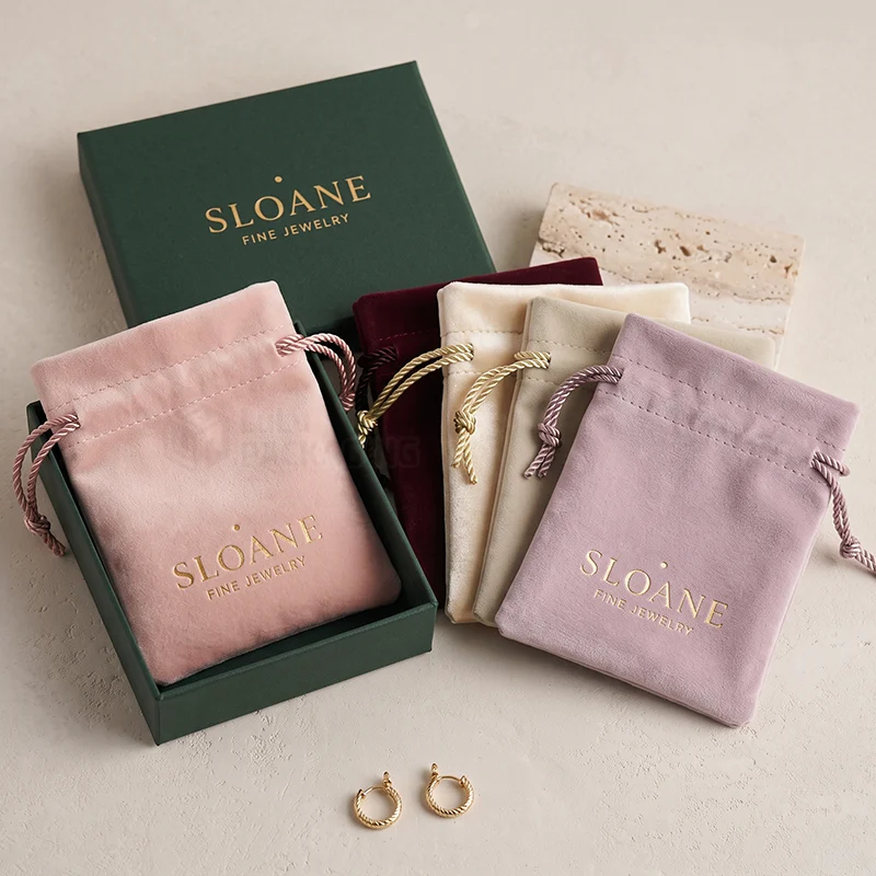 Suede drawstring pouches in pink, burgundy, cream and lilac with a gold logo and a green gift box