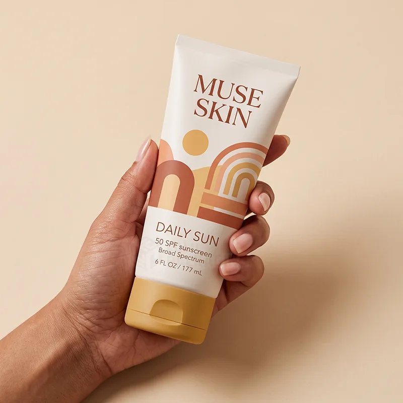 Hand holding a white squeeze tube of sunscreen with an orange and peach arch-pattern label