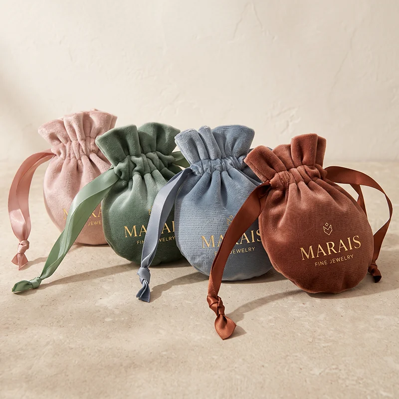 Four round velvet drawstring pouches in blush, sage, blue and rust with satin ribbons and gold logos