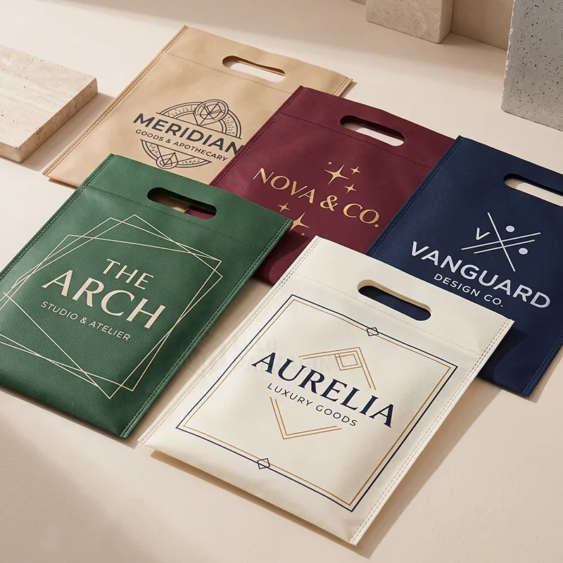 Five flat non woven bags with die cut handles in tan, burgundy, navy, green and cream