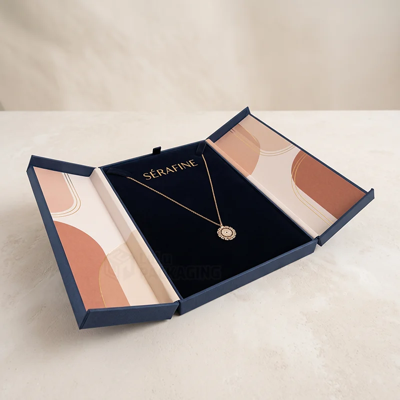 Navy double-door jewellery gift box with printed panels and a gold pendant on dark velvet