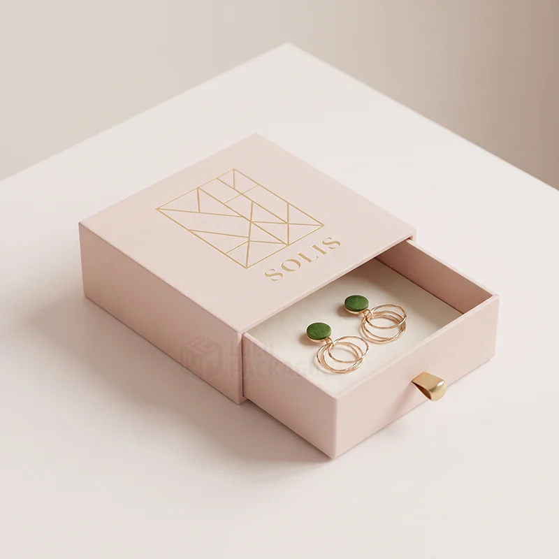 Pale pink drawer earring box with a gold foil logo and green stud hoop earrings