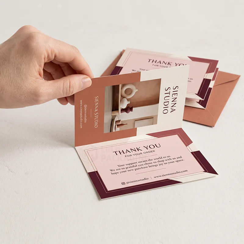 Hand opening a folded insert card with photo panel and thank you message, envelopes and spare cards behind
