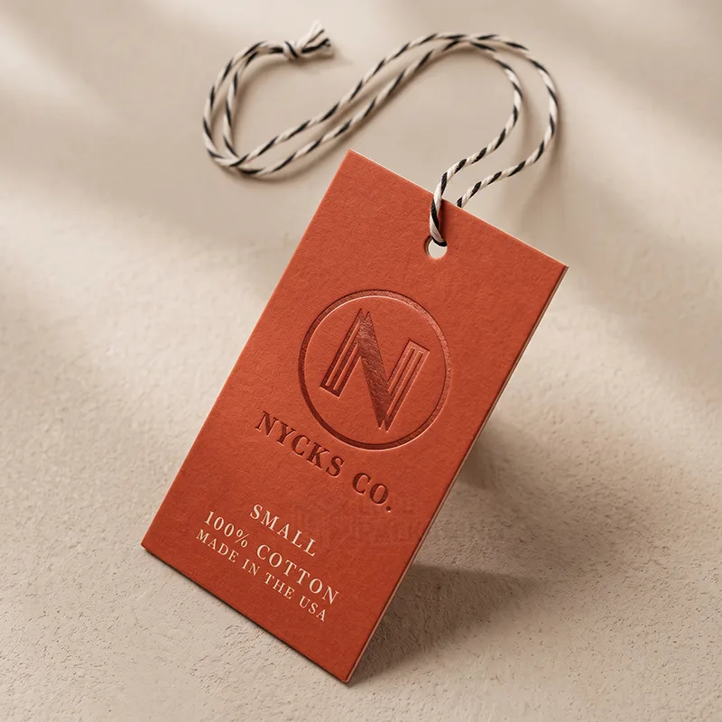 Orange embossed product tag with a round N logo, size and cotton details, and a striped twine string