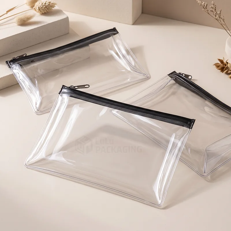 Flat clear PVC zipper pouches with black zippers on a cream surface