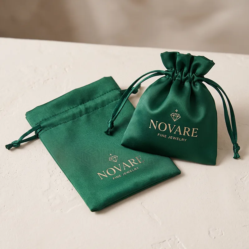Two green satin drawstring jewellery bags with a gold printed logo, one flat and one gathered