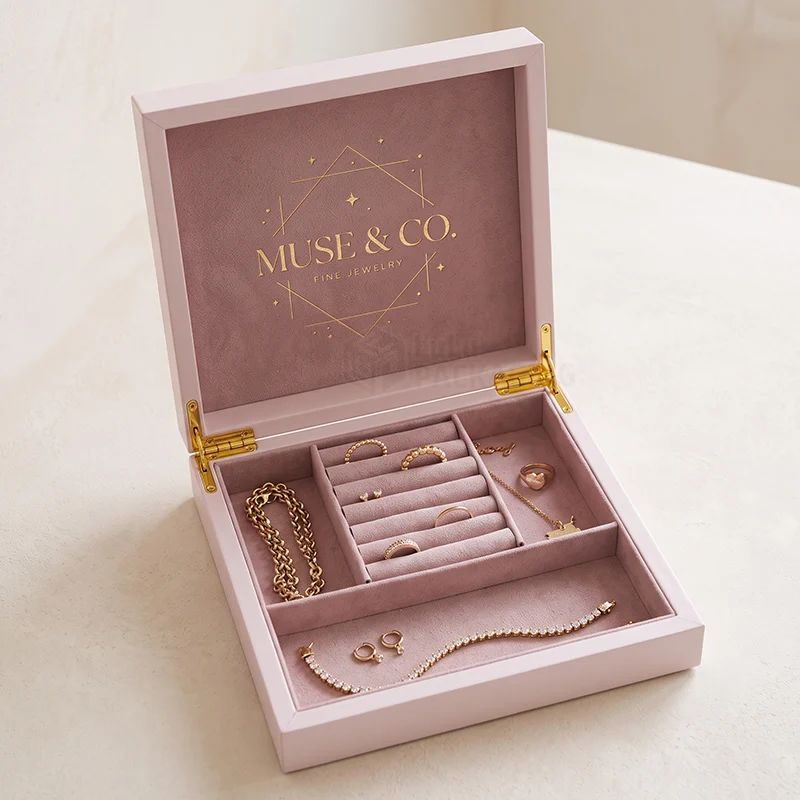 Pink hinged jewellery gift box with a foil logo and velvet compartments full of gold jewellery