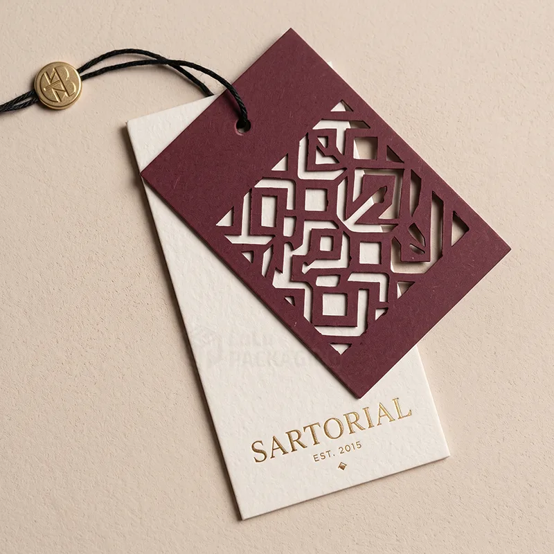 Burgundy tag with a cut-out geometric pattern layered over a cream tag with gold foil Sartorial text