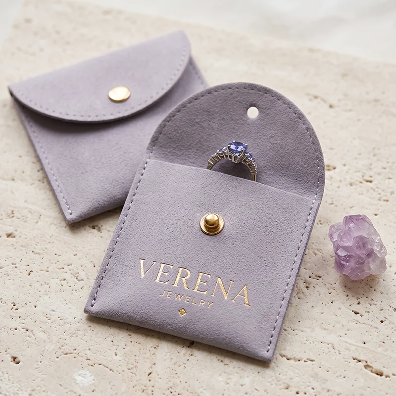 Lilac suede envelope pouch with a gold snap, open to show a ring tucked inside