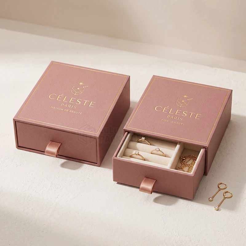 Dusty pink luxury drawer boxes with a gold foil logo, one open showing rings and a chain