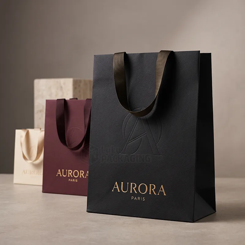 Black luxury paper bag with an embossed logo and satin ribbon handles in front of burgundy and cream bags