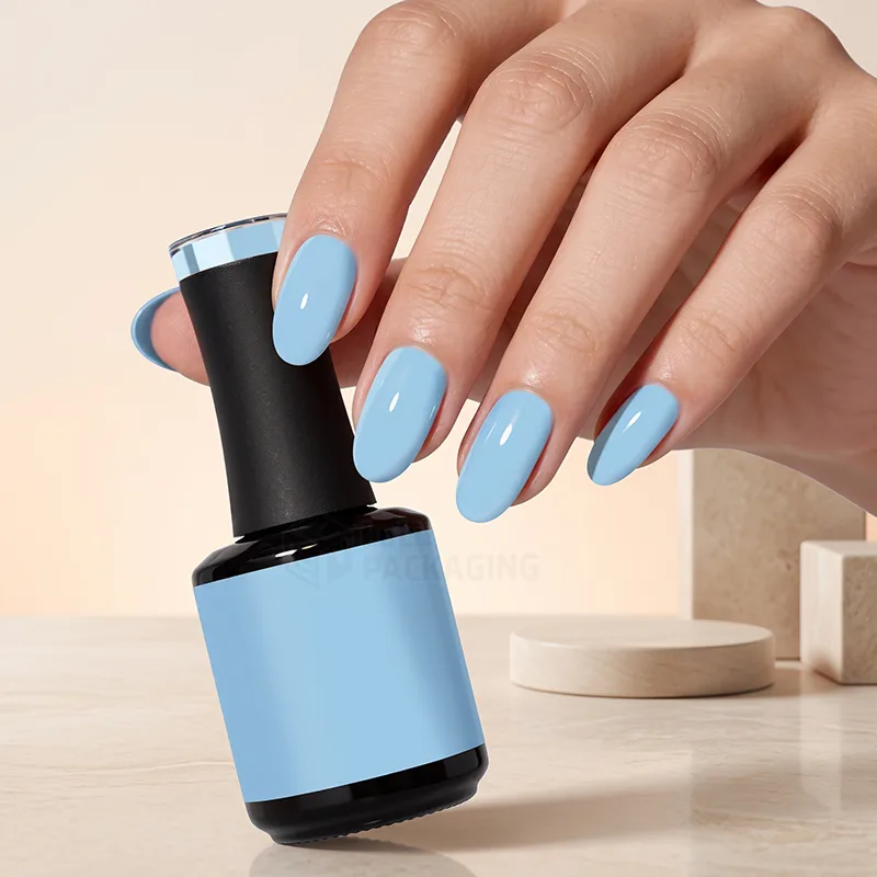 Hand with pale blue nails holding a black nail polish bottle with a blue label