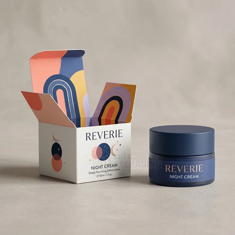 Open white night cream box printed with moon and rainbow arch art beside a navy jar