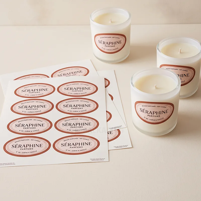 Sheets of oval pink candle labels beside three white candles wearing the same labels