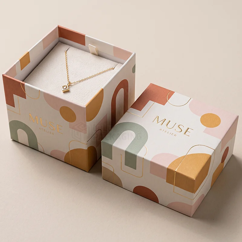 Abstract printed pendant boxes with a gold foil logo, one holding a small gold pendant
