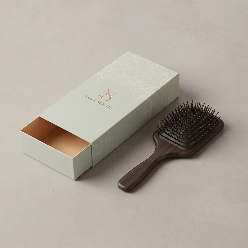Sage drawer comb box with foil logo beside a dark wooden paddle brush