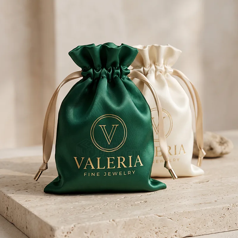 Green and ivory satin drawstring pouches with a gold foil logo and ribbon ties