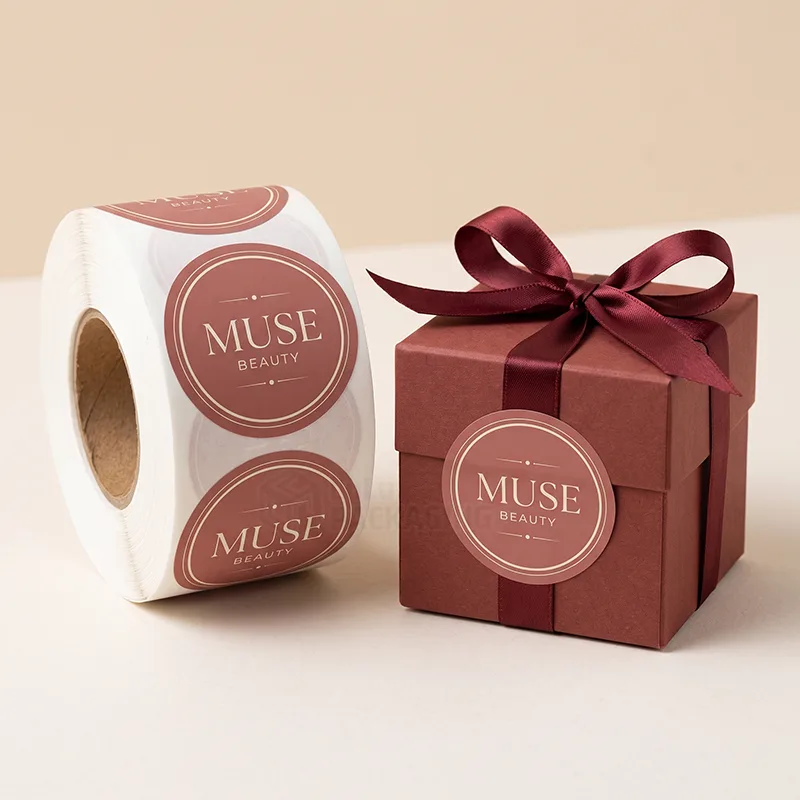 Roll of round burgundy seal stickers next to a red gift box tied with ribbon and closed with a matching seal