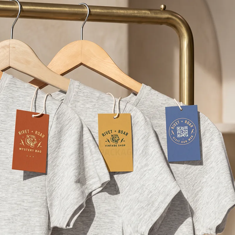 Three coloured product tags with a tiger logo and a QR code hanging on grey t-shirts on a brass rail
