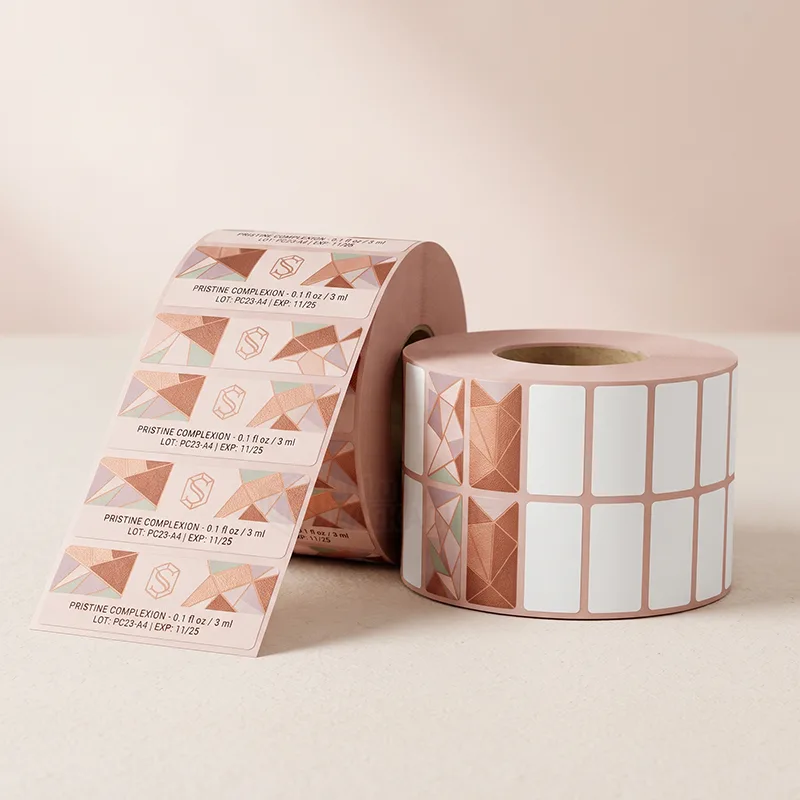 Two rolls of rose gold geometric tube labels with a monogram and lot and expiry text